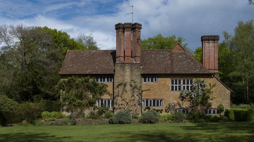 Brick and Stone west elevation of the house at Munstead Wood. Climbing roses and bushy shrubs grow in front of the ground floor.